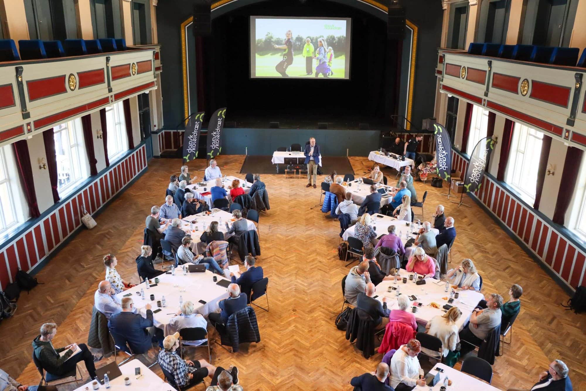 Mennesker sidder ved en masse mindre borde til en konference