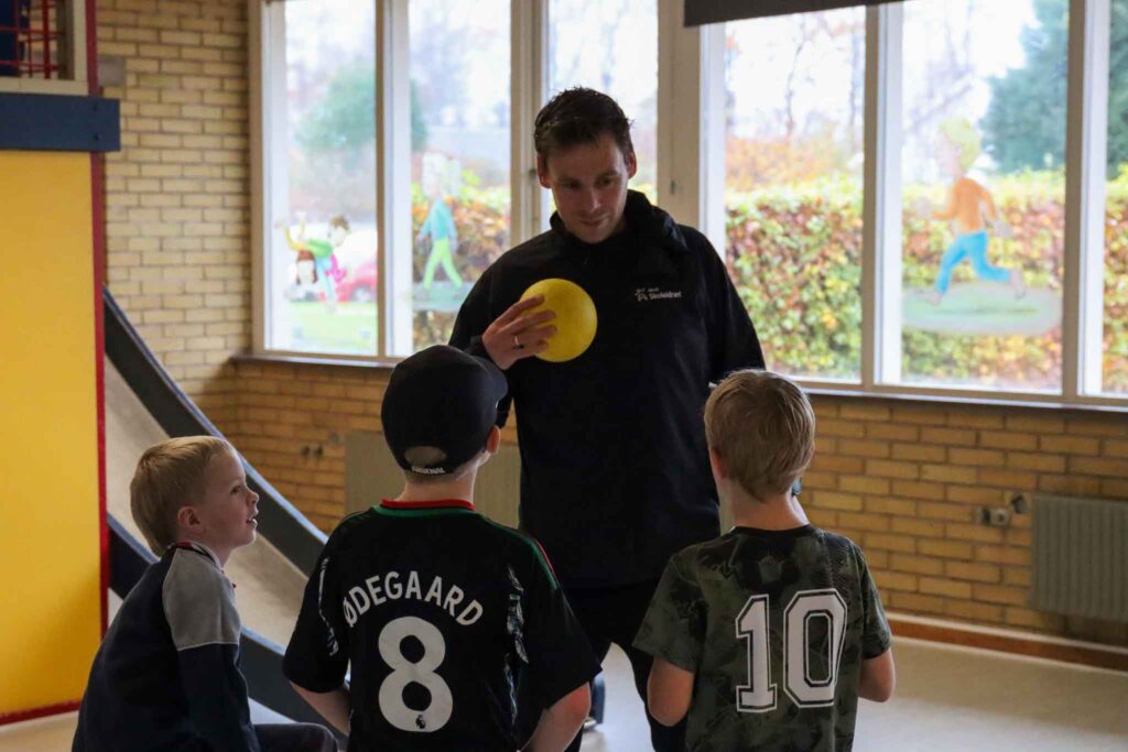 Voksen holder en stikbold. Drenge står klar til at lege.