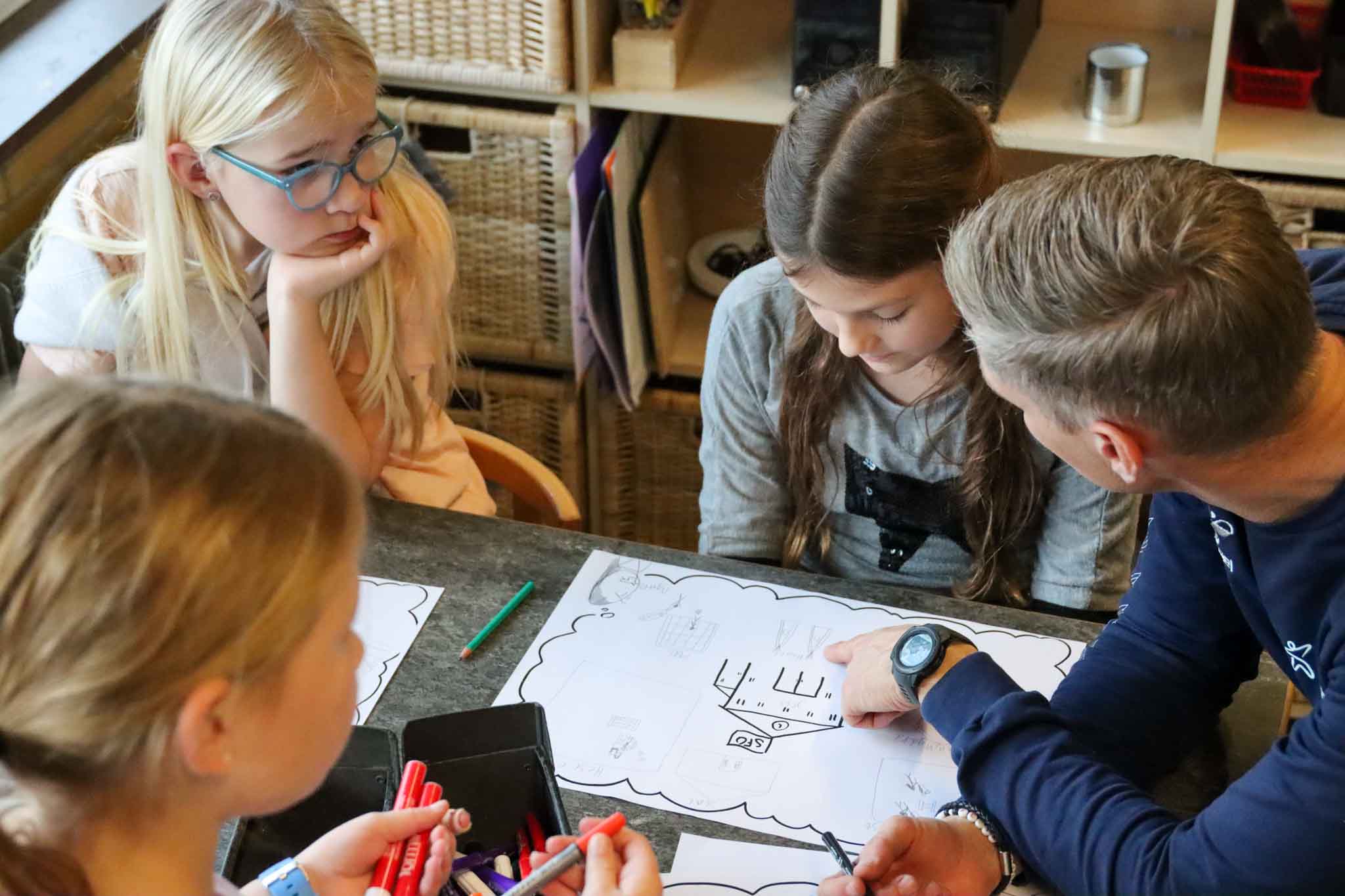 Projektleder sidder med børn og spørger ind til deres tegninger
