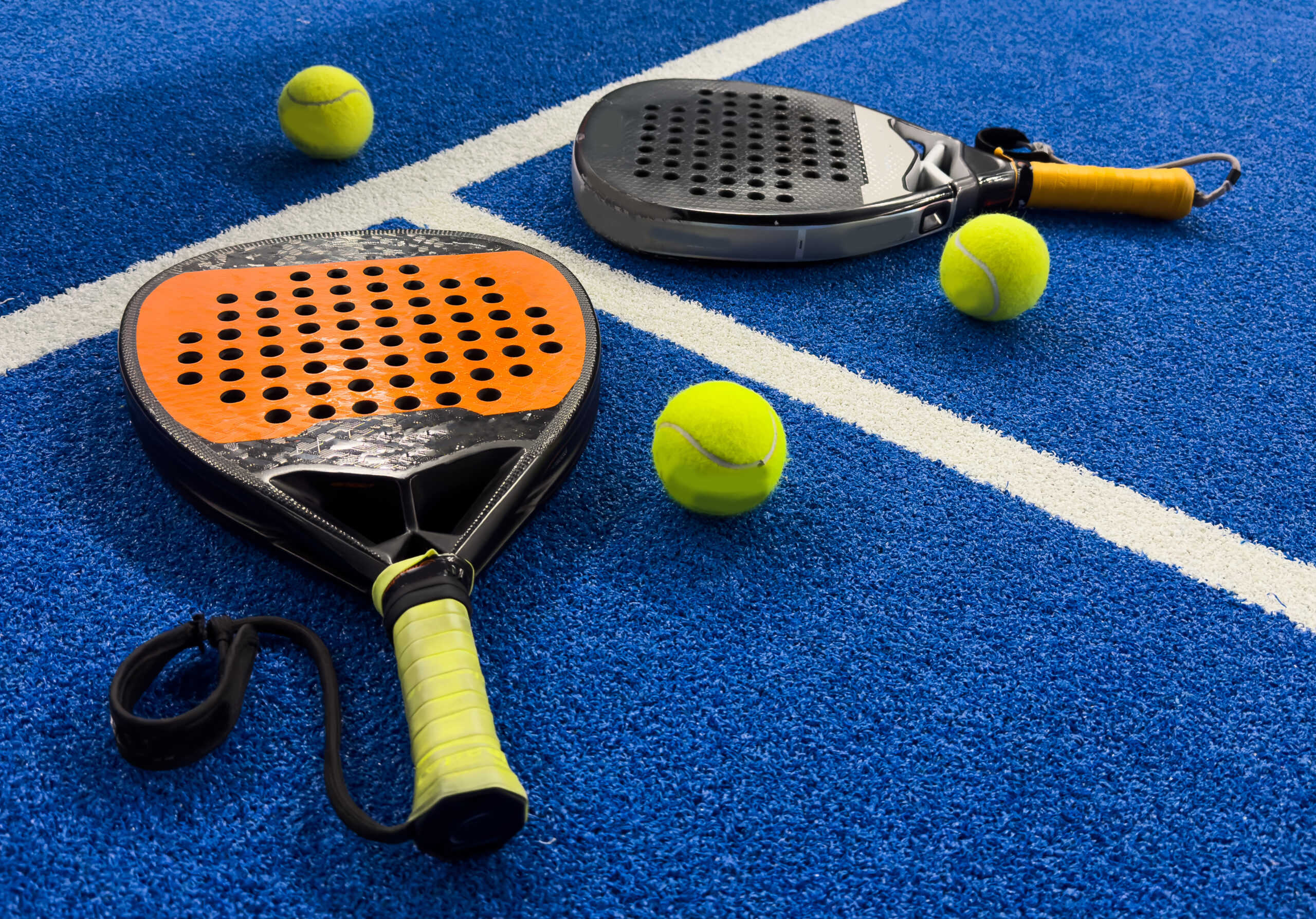 Photo of an orange padel racket and a ball on the ground of a blue outdoor court. Padel concept. Paddle equipment. High quality photo